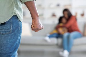 istockphoto-1369137588-612×612 Domestic Violence. Unrecognizable African American Man Threatening Wife And Daughter With His Fist, Scared Mother Embracing Little Girl While Sitting Together On Couch, Selective Focus On Male Hand